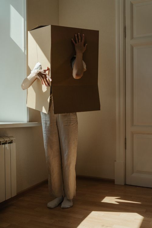 Free Artistic indoor photo of a person creatively posing with a cardboard box, playing with light and shadows. Stock Photo