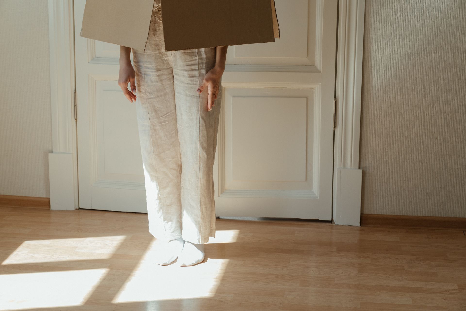 Person in White Pants and White Shoes Standing on Brown Wooden Floor