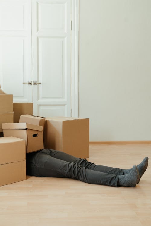 Person in Black Pants Lying on Brown Cardboard Box