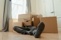 Person in Black Pants Sitting on Brown Cardboard Box