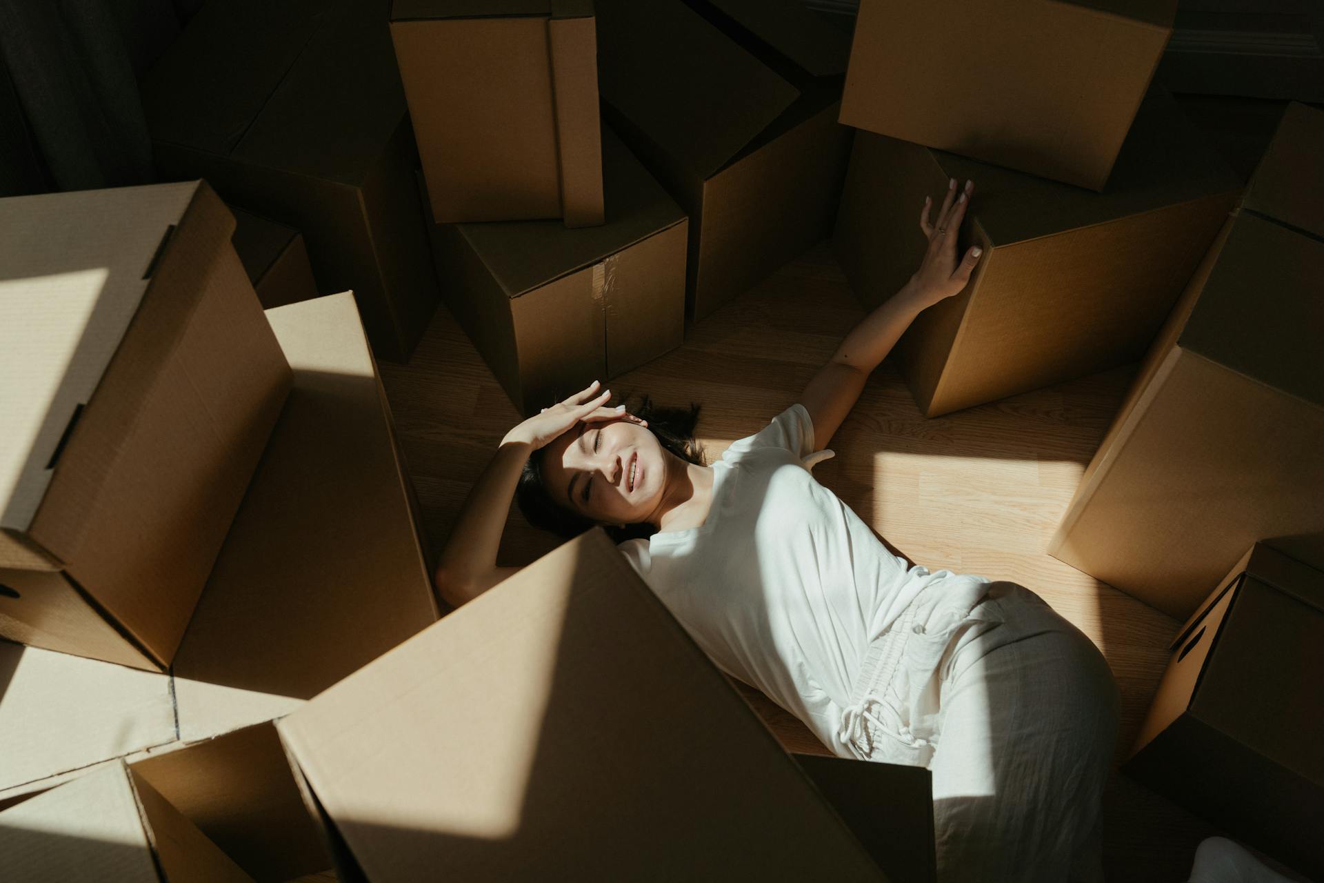 A woman lying among cardboard boxes with dramatic light and shadow. Perfect for moving or relocation themes.