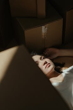 一名妇女躺在成堆的纸板箱中，被柔和的日光照亮