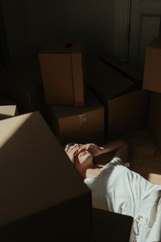 光线昏暗的房间里，一名妇女躺在地板上，周围堆满纸板箱，显得十分疲惫