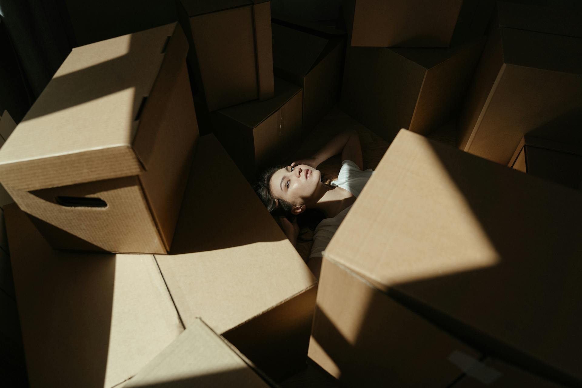 Young woman lying among cardboard boxes in the sunlight, indicating a move-in or relocation.