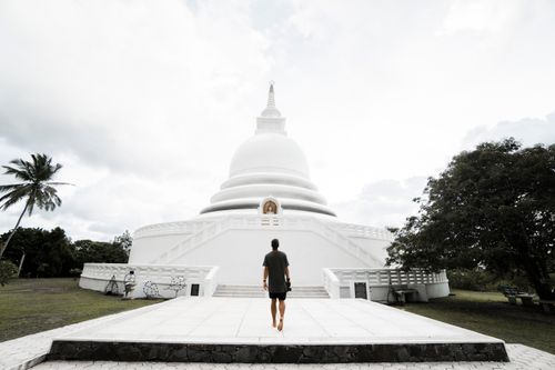 Free Back view full body faceless male tourist in black summer wear strolling on paved path towards scenic white Japanese Peace Pagoda in tropical country on clear day Stock Photo