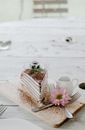 From above composition of sweet pancake cake with whipped cream placed on light wooden board with cutleries and delicate pink flower