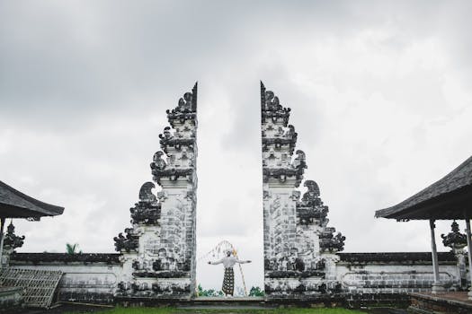 A person stands between the iconic Gates of Heaven at Lempuyang Temple, Bali, under a cloudy sky.