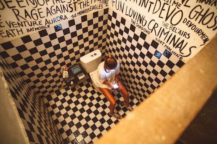 Woman Sitting On Toilet Bowl With Smartphone