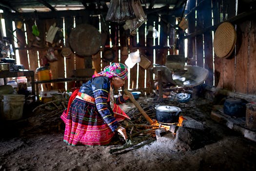 Full body side view of adult focused female in colorful traditional suit moving wood while cooking over fire in old shed
