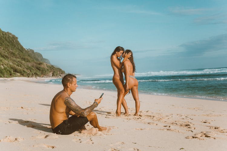 Man Using Smartphone While Sexy Women Kissing On Beach