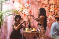Side view happy African American females in stylish dresses taking photos on smartphones of freshly cooked food while having lunch in cozy cafe against painted wall