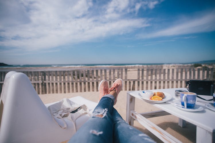 Person Resting On Sunbed With Breakfast On Beach By Sea