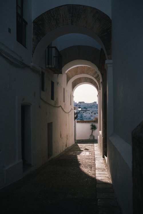 Free A scenic view of a narrow urban passageway framed by arches and shadows in sunlight. Stock Photo