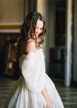 身着优雅白色连衣裙的白人女子在室内微笑着，展现出新娘的优雅