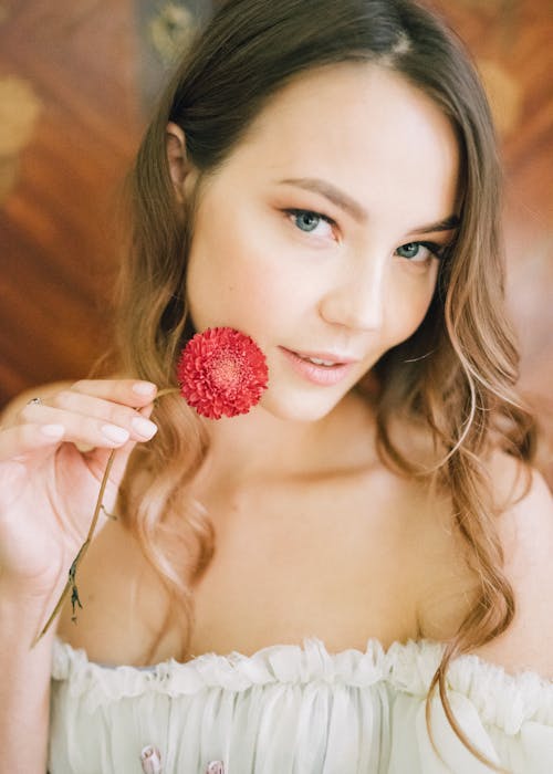 Blue Eyed Woman Holding a Red Flower Near Her Face