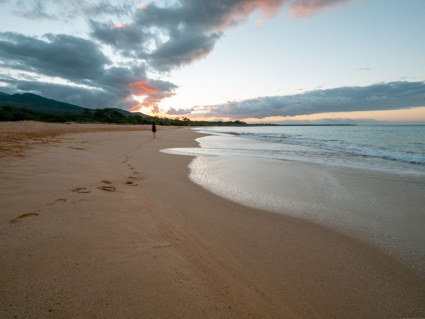 Picturesque scenery of sandy beach with waving ocean under cloudy sky during sunset