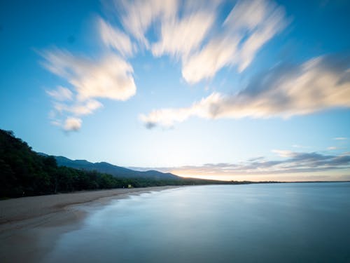 Aerial of picturesque scenery of calm sea and shoreline with green forest and cloudy sky with long exposure