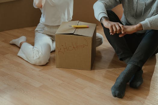 Couple sitting on the floor unpacking boxes in their new home kitchen.