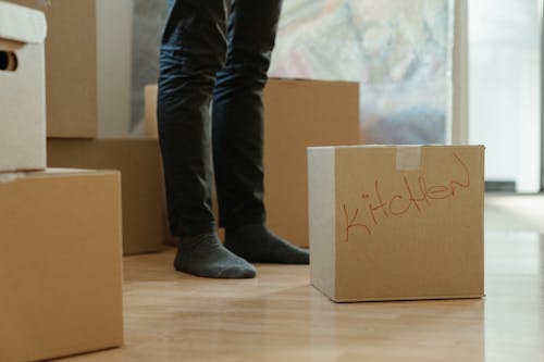 Free Person in Blue Denim Jeans Standing Beside Brown Cardboard Box Stock Photo