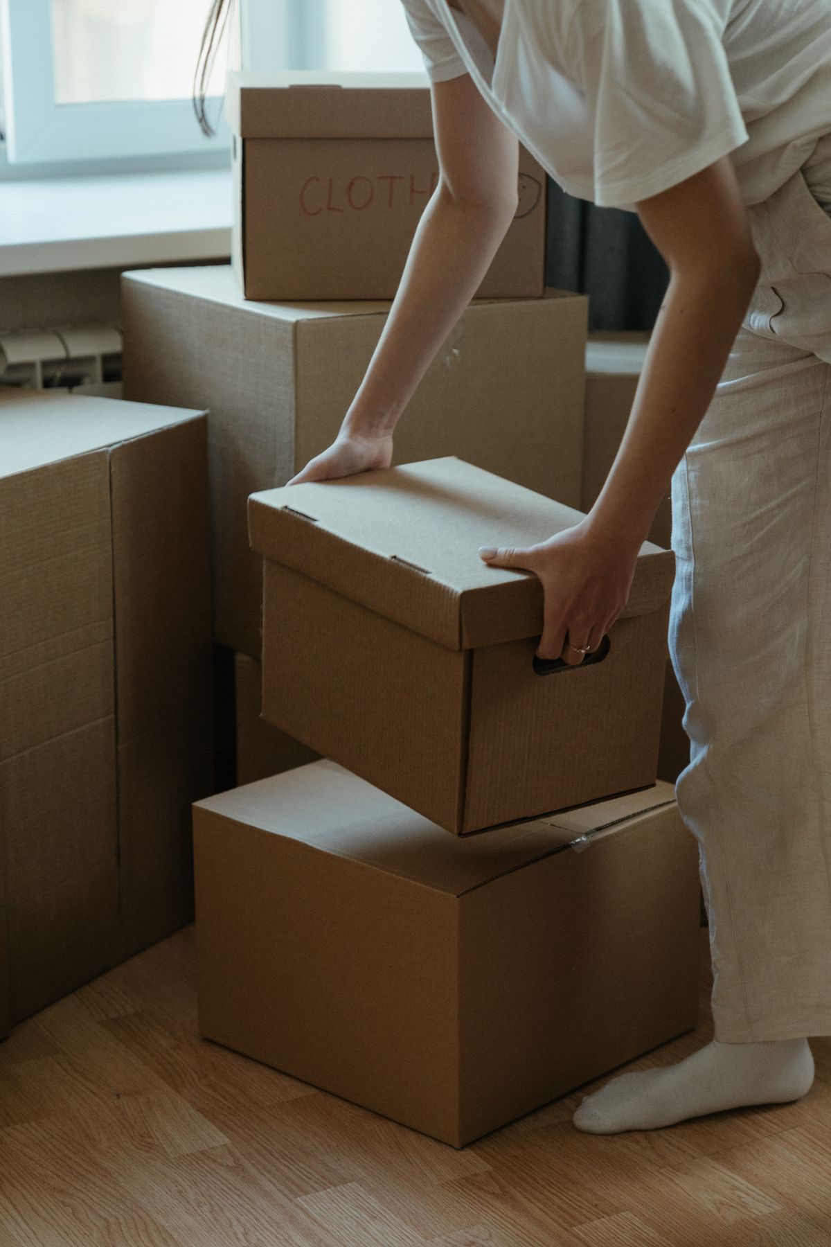 A woman packing cardboard boxes in her new apartment, symbolizing moving and relocation. Illustrative editorial photograph.