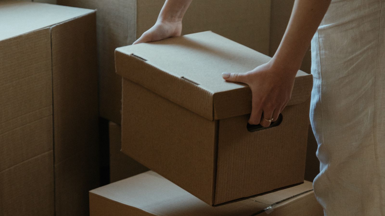 A person lifting a cardboard box beside other packed boxes