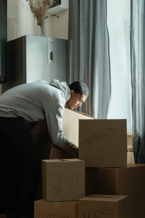 Free A young man in a hoodie packs cardboard boxes while moving into a new apartment. Stock Photo