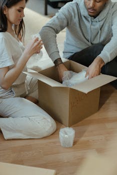 A couple unpacking cardboard boxes in their new home, focusing on kitchen items.