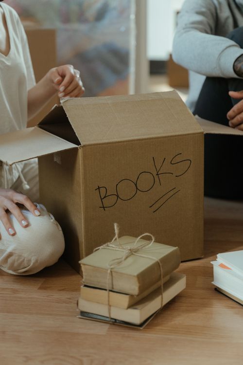 Free Cardboard box labeled 'books' being unpacked on a wooden floor, symbolizing moving and new beginnings. Stock Photo