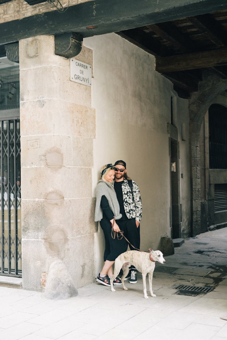 A Couple Leaning Against A Wall Beside A Dog