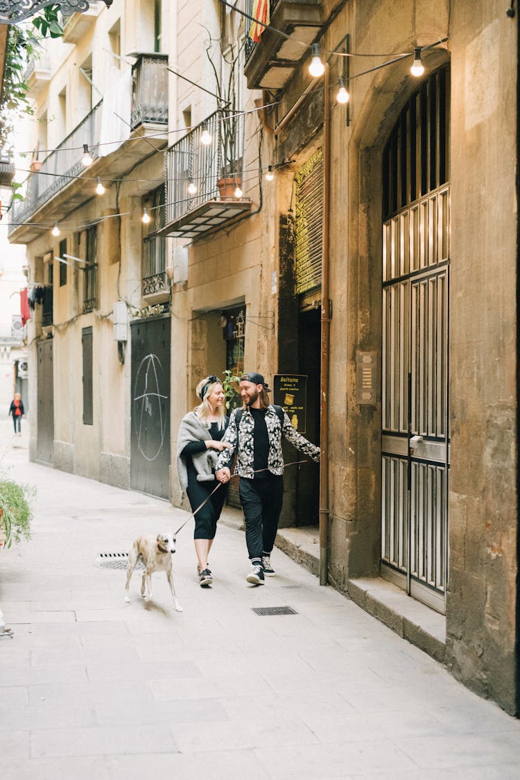 A Couple Walking With A Dog On A Narrow Street