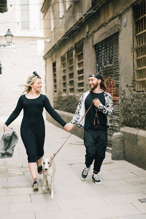 Happy Couple In Black Clothes Walking the Dog While Holding Hands