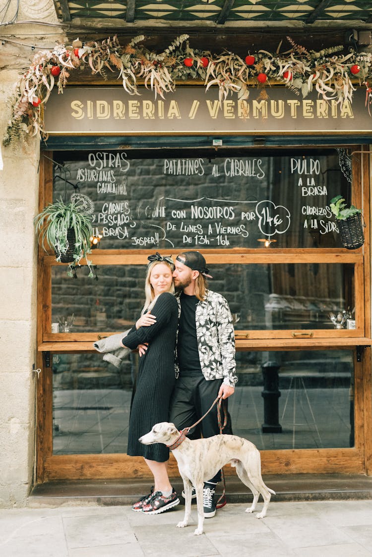  A Romantic Couple Cuddling In Front Of A Store With A Dog