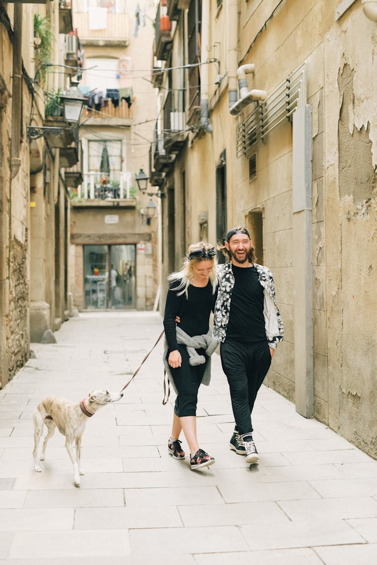 A Couple Walking On The Street Together With Their Pet Dog