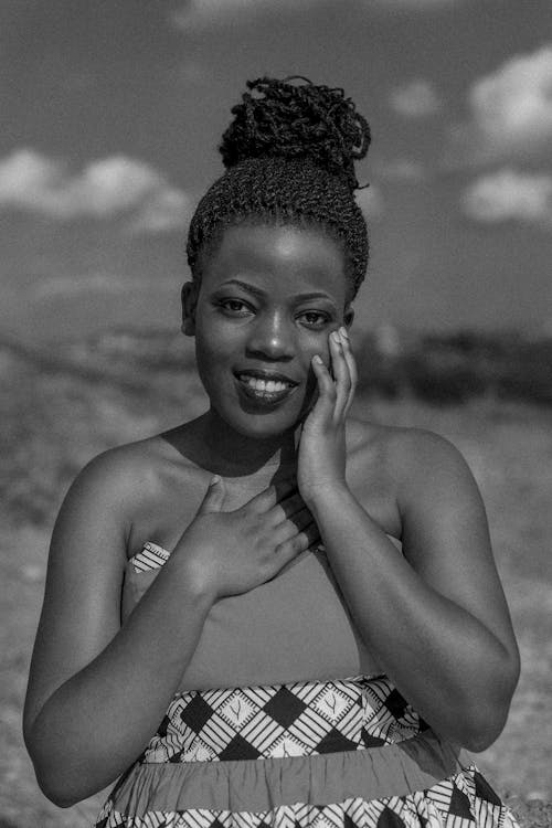 Free Black and white African American female with bare shoulders holding hands on face and chest while gently smiling at camera Stock Photo