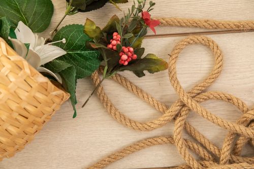 Free A close-up of a woven basket with artificial flowers alongside a decorative rope on a wooden surface. Stock Photo