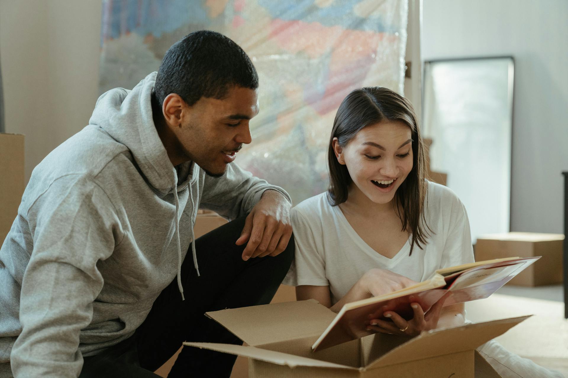 A couple happily unpacking boxes and reading together in their new home, symbolizing a fresh start.