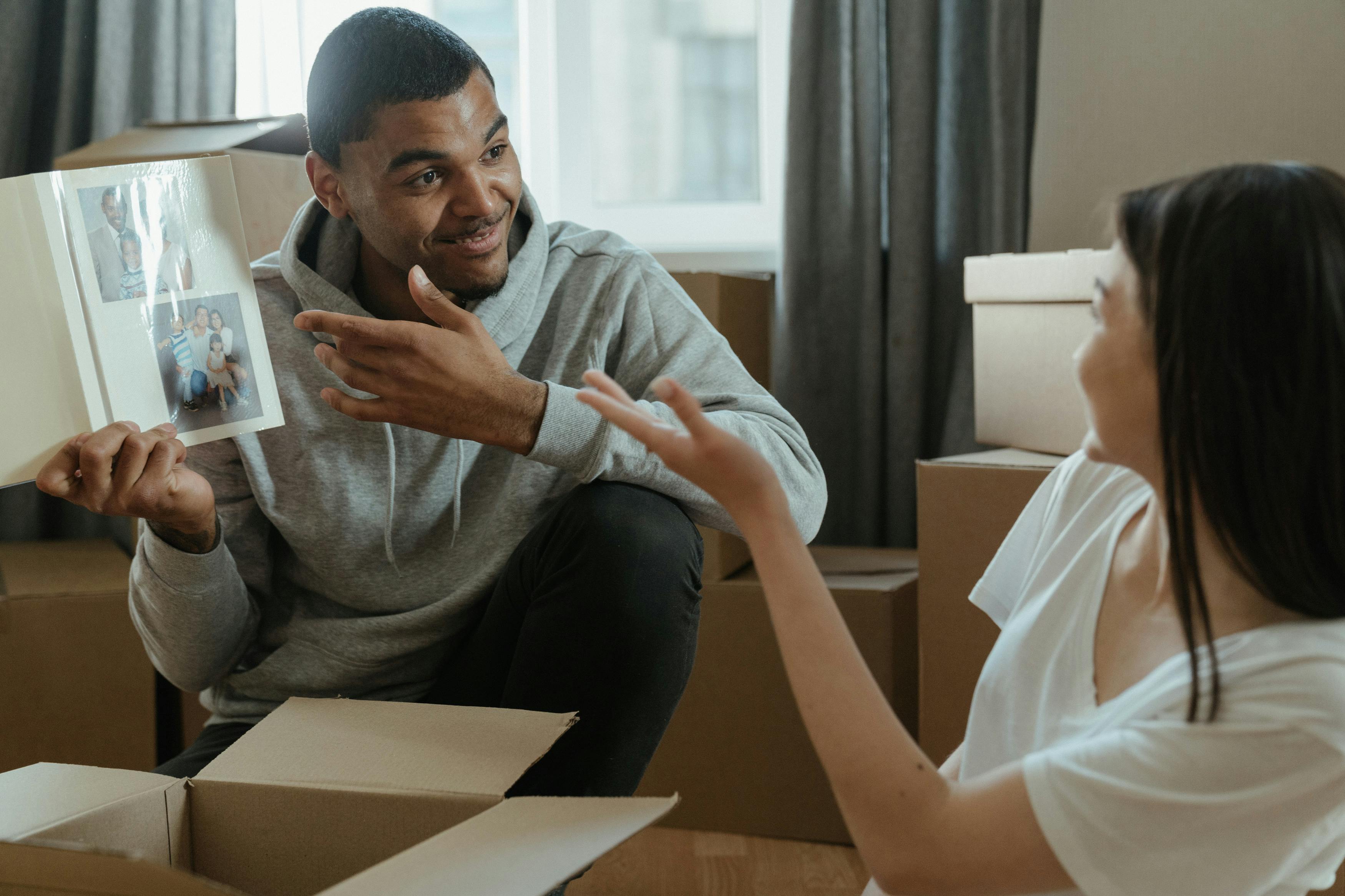 A couple shares memories from a photo album while unpacking boxes in their new home.