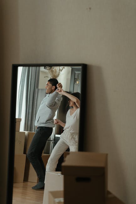 A joyful couple celebrates moving into their new apartment by dancing among unpacked boxes.