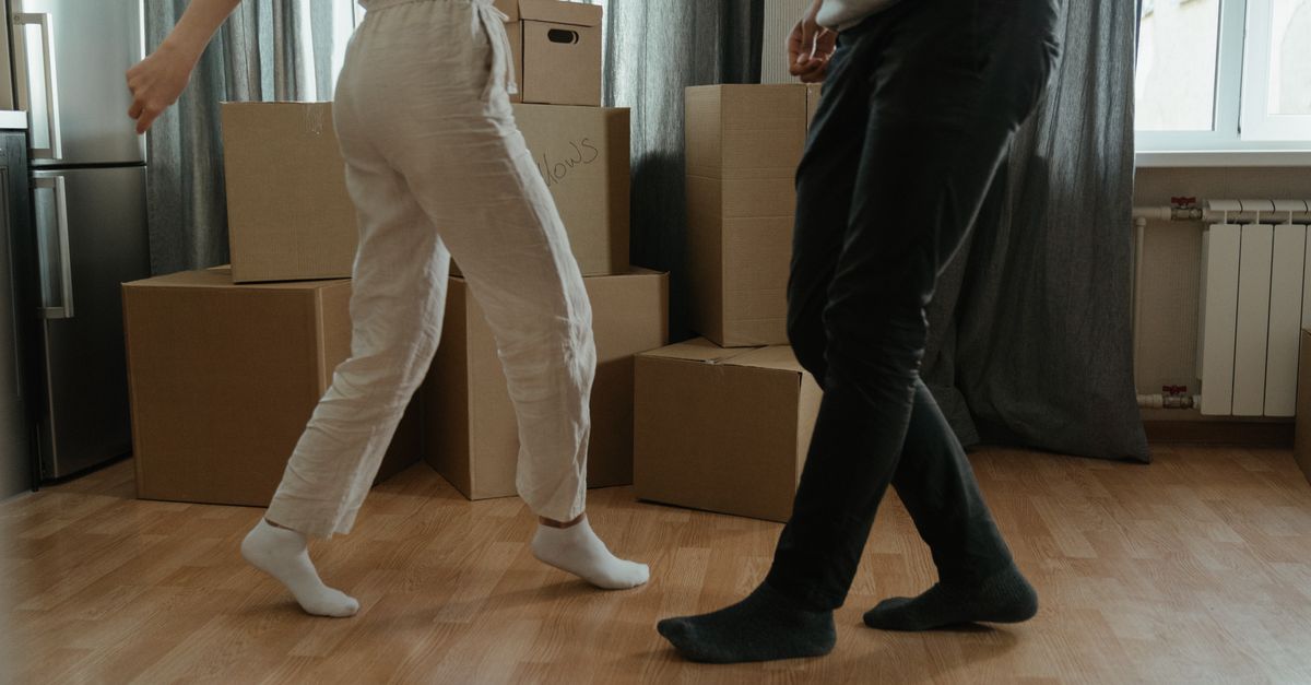 Two people dance joyfully amidst moving boxes in their new home.