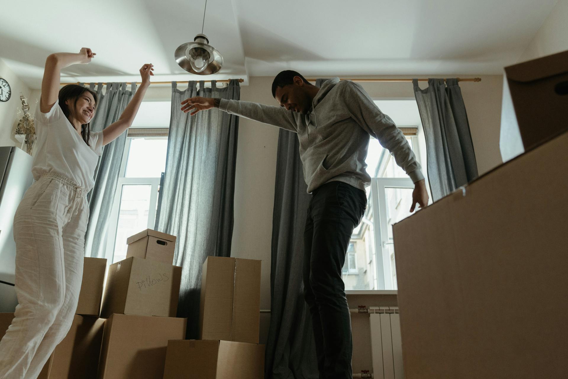 Man in Gray Long Sleeve Shirt and Black Pants Standing Beside Brown Cardboard Boxes