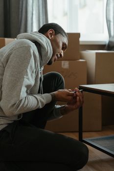 一名男子正在他的新公寓里组装桌子，周围堆满了纸板箱