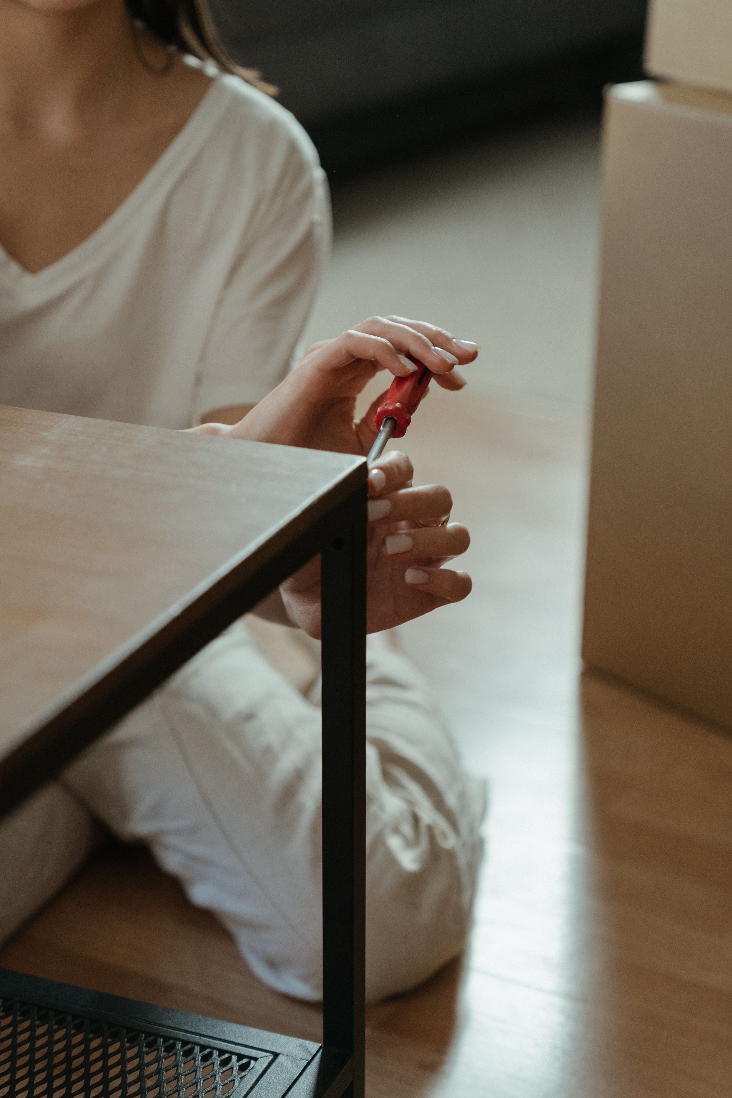 A woman using a screwdriver while assembling furniture indoors