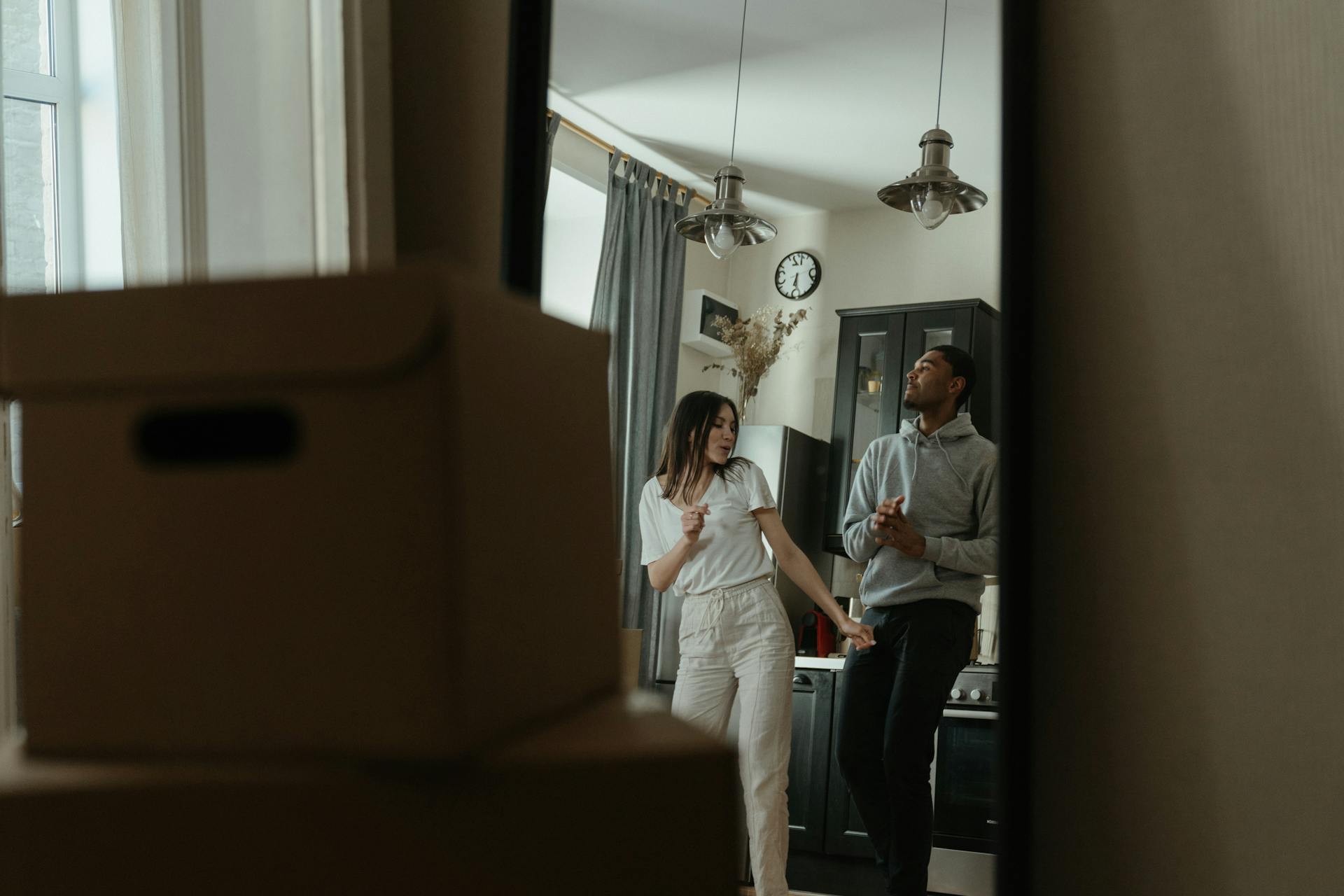 Happy couple dancing in their new home with cardboard boxes around them.