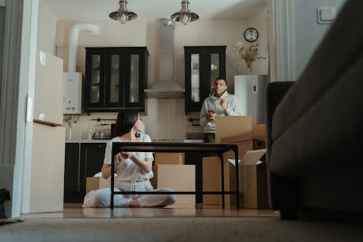 A couple is seen unpacking boxes in their new apartment, setting up their kitchen area.