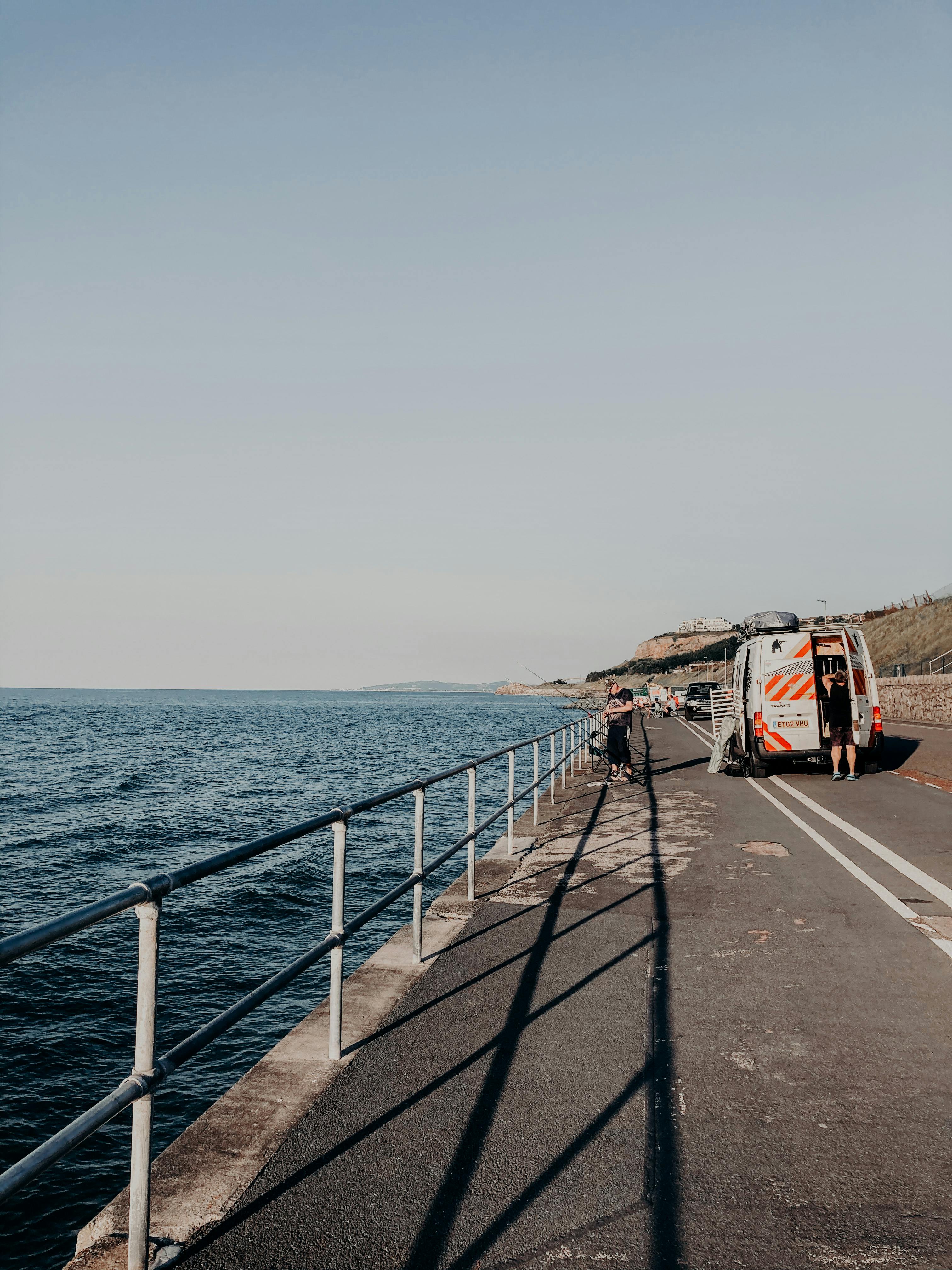 Road works on asphalt roadway along rippling endless sea under cloudless sky at daytime