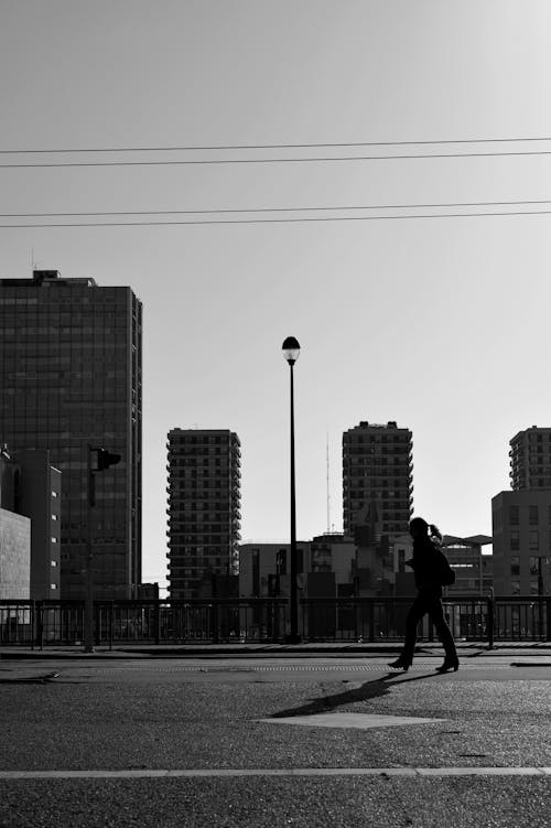 Black and white silhouette of anonymous female walking along asphalt roadway in city