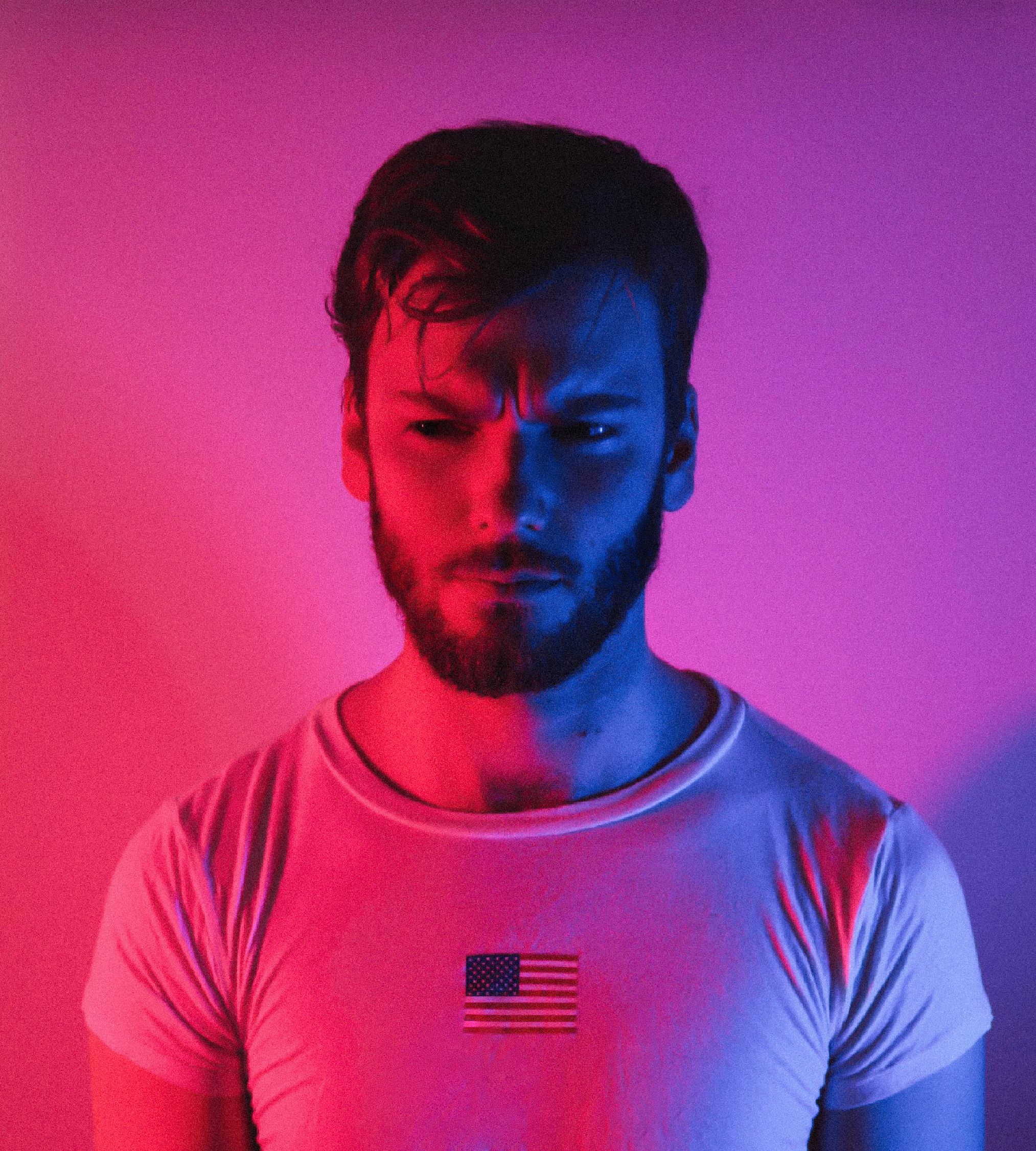 Bearded man in neon pink and blue lights wearing an American flag shirt.