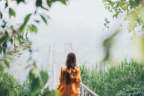 Free High angle back view of unrecognizable female in dress walking along boardwalk to pond Stock Photo