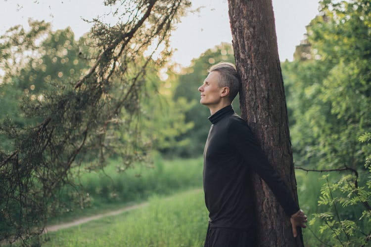 Young Man Standing Near Tree Trunk In Forest