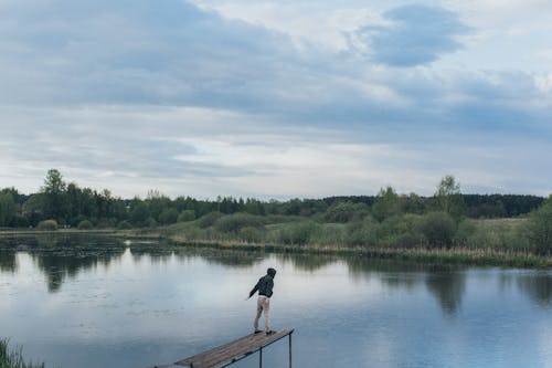 Man standing on edge of wooden pier near lake